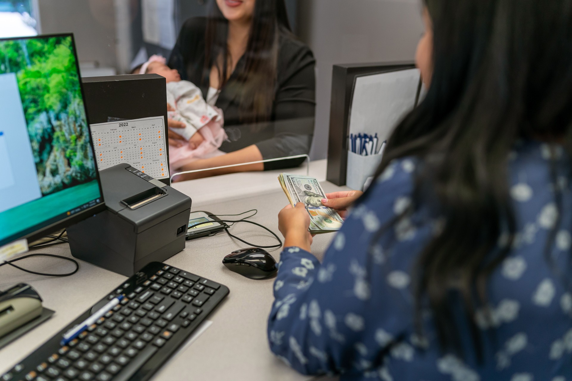 Bank teller counting cash for female customer holding a baby